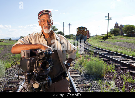 African American man with film camera near railroad tracks Stock Photo