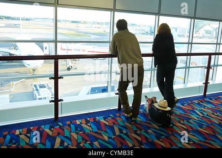 Two passengers look out of a window while waiting for a plane at Gatwick Airport, London Stock Photo