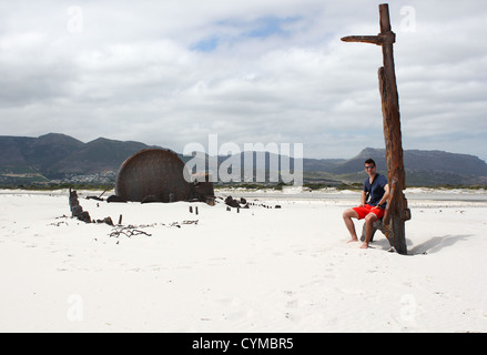 Man sitting at Shipwreck Kakapo at the beach of kommetjie with upcoming storm in the background Stock Photo