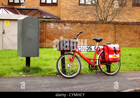 Postman's bike resting on a street sign near a postal deposit box in Bradley Stoke Bristol, England, UK