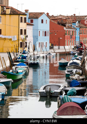 Tranquil view across a canal in Burano, Venice, showing brightly-painted houses and boats with their reflections in the water Stock Photo