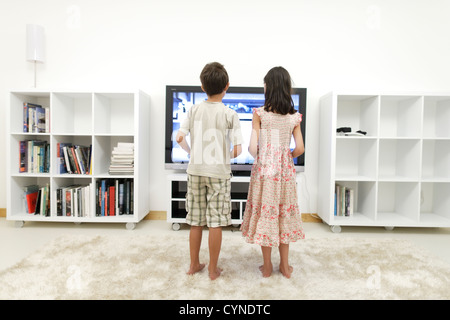 Boy and girl play video games on large 55 inch flat-screen television in white room Stock Photo