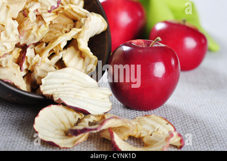 Dried apples chips in ceramic bowl with fresh red apples on table Stock Photo