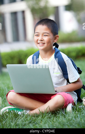 Smiling schoolboy sitting on the lawn with laptop Stock Photo