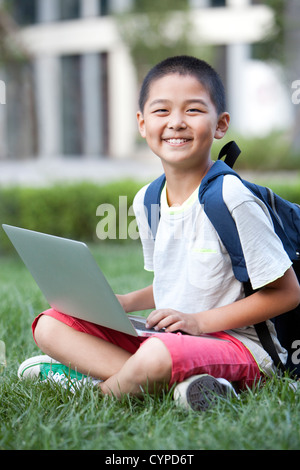 Smiling schoolboy sitting on the lawn with laptop Stock Photo