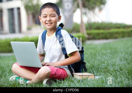 Schoolboy using laptop with books beside Stock Photo