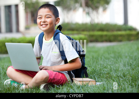 Schoolboy using laptop with books beside Stock Photo