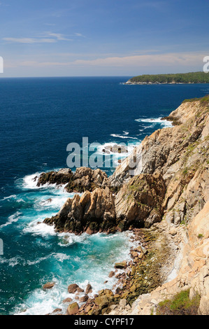 Mexico, Oaxaca, Huatulco, Rocky cliff edge with waves breaking on rocks below and Bahia Maguey on the Pacific coast. Stock Photo