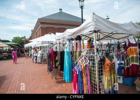 Eastern Market Clothing Vendor Washington DC | WASHINGTON DC — Colorful clothing hangs from racks at a vendor's stall at Eastern Market, part of the weekend outdoor markets that expand the Capitol Hill institution beyond its historic brick building. The South Hall at the core of the complex was designed by Adolf Cluss and completed in 1873, establishing what has become the oldest continuously operating public food market in Washington DC. On weekends, the indoor food market is joined by outdoor vendors selling clothing, jewelry, art, antiques, and other merchandise along 7th Street SE, transfo Stock Photo