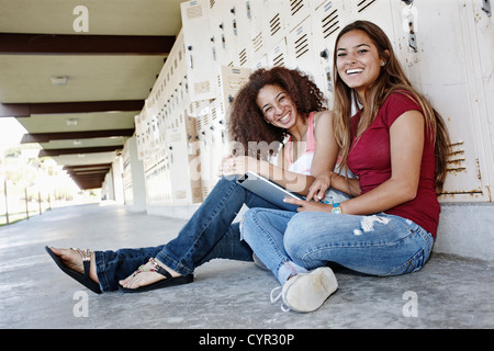 School friends sitting near lockers with digital tablet Stock Photo