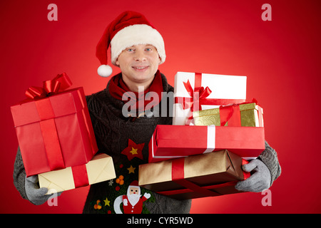 Portrait of happy man in Santa cap holding giftboxes and smiling at camera Stock Photo