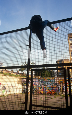 An unidentified youth is seen climbing over a high security fence into a derelict basketball court in the Notting Hill area. Stock Photo
