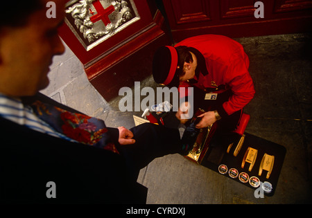 A businessman stands over a Victorian-style shoe-shiner in a corner of Leadenhall Market in the City of London. Stock Photo