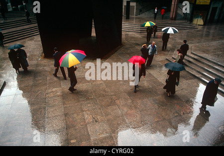 Londoners from a break from their office jobs, take a walk in the rain at Broadgate in the City of London. Stock Photo