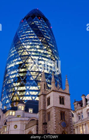 Swiss Re Building 30 St Mary Axe also known as the Gherkin at night with tower of St Andrew Undershaft City Of London England UK Stock Photo
