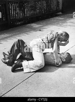 Two young boys fighting on the sidewalk Stock Photo