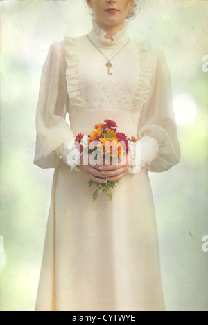 a woman in a victorian dress on a meadow with a bouquet of flowers Stock Photo