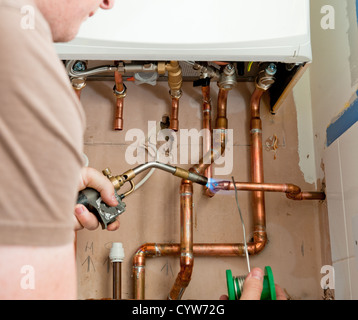 Close up of a real life situation where a heating engineer is soldering copper pipes to a new central heating boiler. Stock Photo