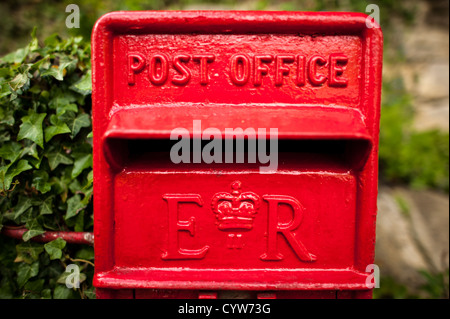 Royal Mail Red Post Box Elizabeth II Cypher Painswick England | PAINSWICK, United Kingdom — A cast-iron Royal Mail pillar box bears the EIIR cypher and crown, marking it as one of thousands installed during the reign of Queen Elizabeth II. The embossed "POST OFFICE" lettering above the slot identifies its original operator, and pillar boxes of this Post Office design have stood on British streets in largely unchanged form since the 1850s. Stock Photo
