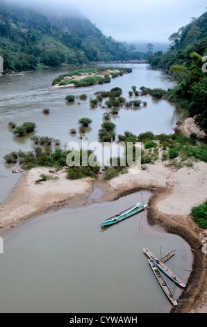 NONG KHIAW, Laos - In the foreground, wooden canoes are moored on riverbank of Nam Ou (River Ou) in Nong Khiaw in northern Laos. The sandy bottom of the river means that the current creates small, sandy islands and protected inlets on the river. Stock Photo