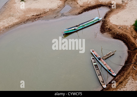 NONG KHIAW, Laos - Wooden canoes moored on riverbank of Nam Ou (River Ou) in Nong Khiaw in northern Laos. The sandy bottom of the river means that the current creates small, sandy islands and protected inlets on the river. Stock Photo