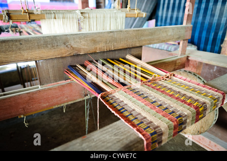 Guatemalan Textiles At Casa Del Tejido Antiguo Antigua Guatemala | ANTIGUA GUATEMALA, Guatemala — Multicolored warp threads stretch across a traditional wooden loom at Casa del Tejido Antiguo, where artisans demonstrate backstrap and foot-loom weaving techniques used across Guatemala's Maya highlands. The close view shows the woven fabric taking shape, thread by thread, on a craft passed down through generations of indigenous weavers. Stock Photo