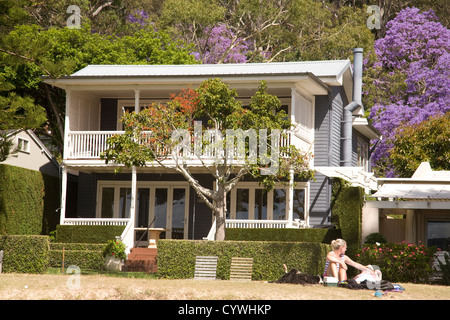 blonde lady relaxes on the beach in front of a large detached australian home Stock Photo