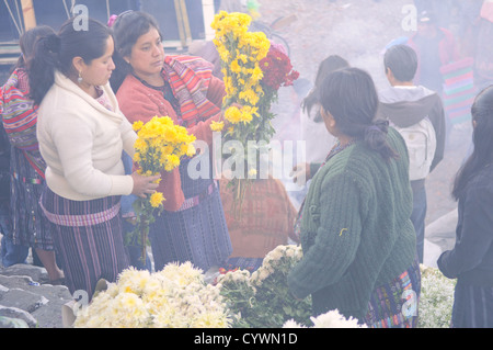 CHICHICASTENANGO, Guatemala - Women selling flowers in the Chichicastengo market. They are on the front steps of Santo Tomas Church and the smoke is from local Maya prayer leaders (known as chuchkajaues) burning incense and copal resin. Chichicastenango is an indigenous Maya town in the Guatemalan highlands about 90 miles northwest of Guatemala City and at an elevation of nearly 6,500 feet. It is most famous for its markets on Sundays and Thursdays. Stock Photo