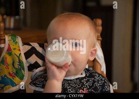 Baby sitting in high chair feeding himself a bottle Stock Photo