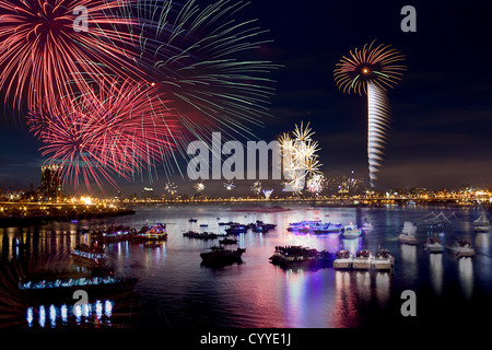 Fire works firing up into the sky with a boat on a river below them, with a reflection on the water Stock Photo