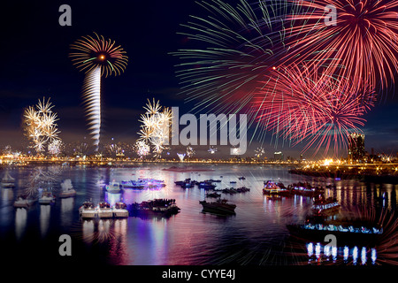 Fire works firing up into the sky with a boat on a river below them, with a reflection on the water Stock Photo
