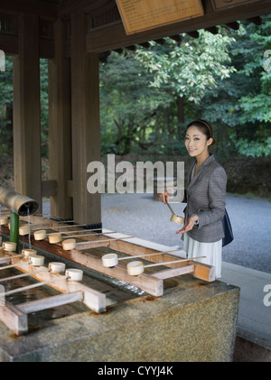 Beautiful young Japanese woman visiting Meiji Jingu Shrine, Tokyo. At the purification trough (chōzuya or temizuya) Stock Photo