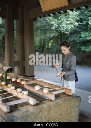 Beautiful young Japanese woman visiting Meiji Jingu Shrine, Tokyo At the purification trough (chōzuya or temizuya) Stock Photo