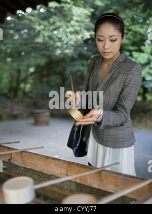 Beautiful young Japanese woman visiting Meiji Jingu Shrine, Tokyo. At the purification trough (chōzuya or temizuya) Stock Photo