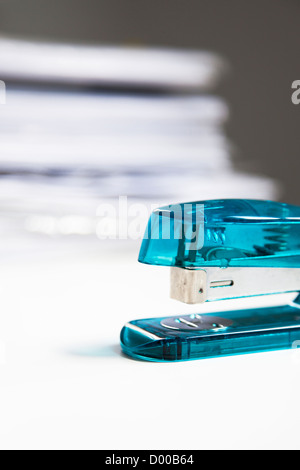 Blue stapler on table with stack of papers in background Stock Photo