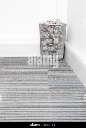 Wastebasket full of crumpled paper in corner on carpet floor in room Stock Photo