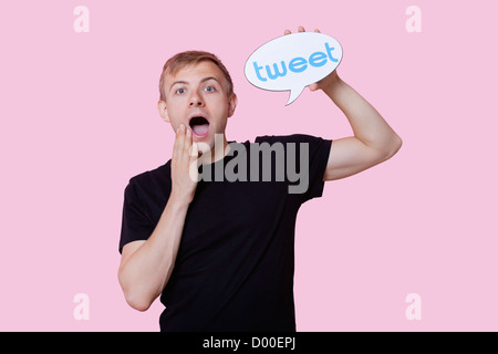 Portrait of surprised young man holding tweet bubble against pink background Stock Photo