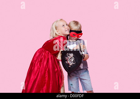 Happy young girl in princess costume hugging boy pretending to be her hero over pink background Stock Photo