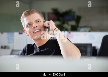Thoughtful young man looking away while using cell phone at office Stock Photo