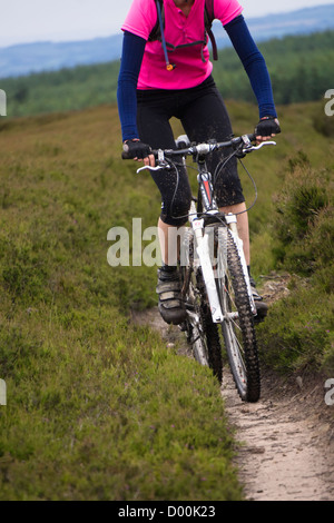 A woman riding her mountain bike through the heather moorlands near Blanchland in Northumberland.