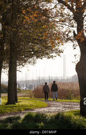 couple walking away through autunm trees in the sunlight with the tower of Fawley power station in the distance Stock Photo