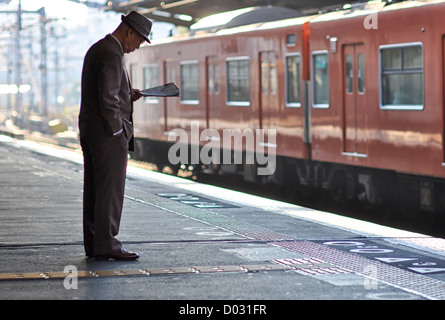 An elderly man reading a newspaper while waiting for a train. Stock Photo