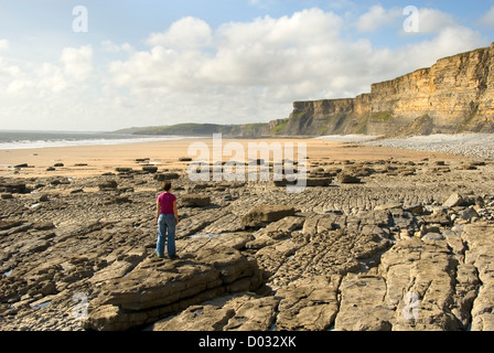Woman standing on a rock looking at the beach and the cliffs, close to Nash Point, Glamorgan Heritage Coast, Wales, UK Stock Photo