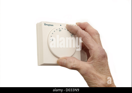 elderly woman lowering the thermostat on the central heating control to combat global warming and climate change Stock Photo