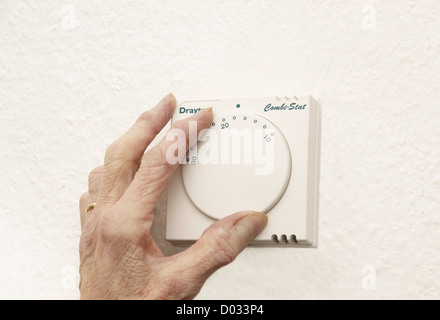 elderly woman lowering the thermostat on the central heating control to combat global warming and climate change Stock Photo