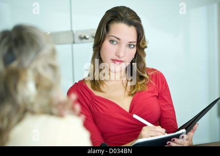 Woman in bright red top taking notes in a meeting. Stock Photo
