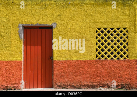 Orange door on a highly textured orange and yellow stucco wall in Mexico. Stock Photo