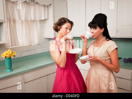 Two retro-styled women drinking coffee in kitchen Stock Photo