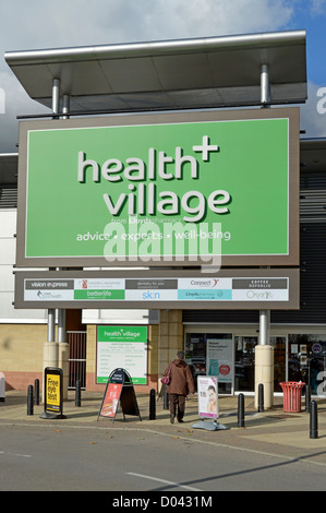 Woman shopper walking towards Health + Village run by Lloyds Pharmacy offering a range of healthcare services Stock Photo