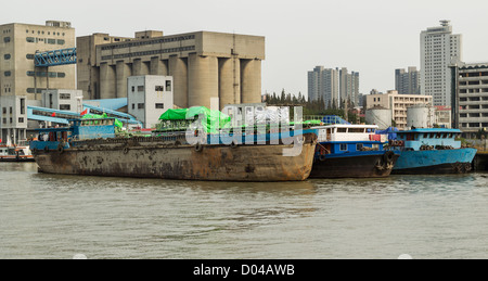 Old Chinese cargo ship docked near storage building on Huangpu River Stock Photo